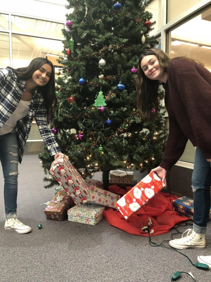 Junior Alyssa Battani and junior Sophia Asta place their wrapped gifts under the Christmas tree.