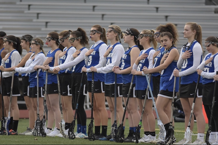 The womens varsity lacrosse team honoring the National Anthem at a game. 