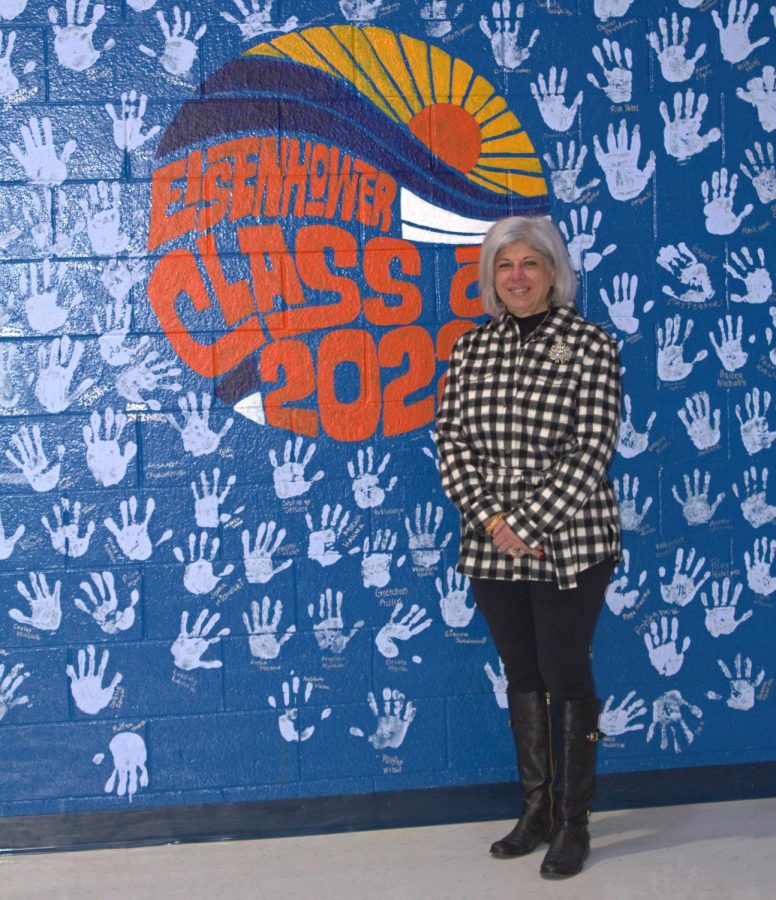  Assistant to the Principal Alicia Singer stands alongside the dedicated mural to the 2022 graduating class. “My love for education was so strong but couldn’t transition into the K-12 world- I did not have a teaching certificate yet,” Singer said. She was very glad to achieve the opportunity to meet so many great people during her last two decades at Eisenhower.