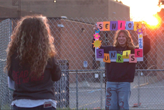  Capturing the moment, seniors Abigail Handsy and Sophia Tripi take pictures under the senior sunrise sun. “I spent hours making the sign for this event and I am happy that the pictures turned out good. I also liked how all my friends asked to use it, it felt good,” Tripi said. Seniors will close their senior year with a senior sunset in late May. 

